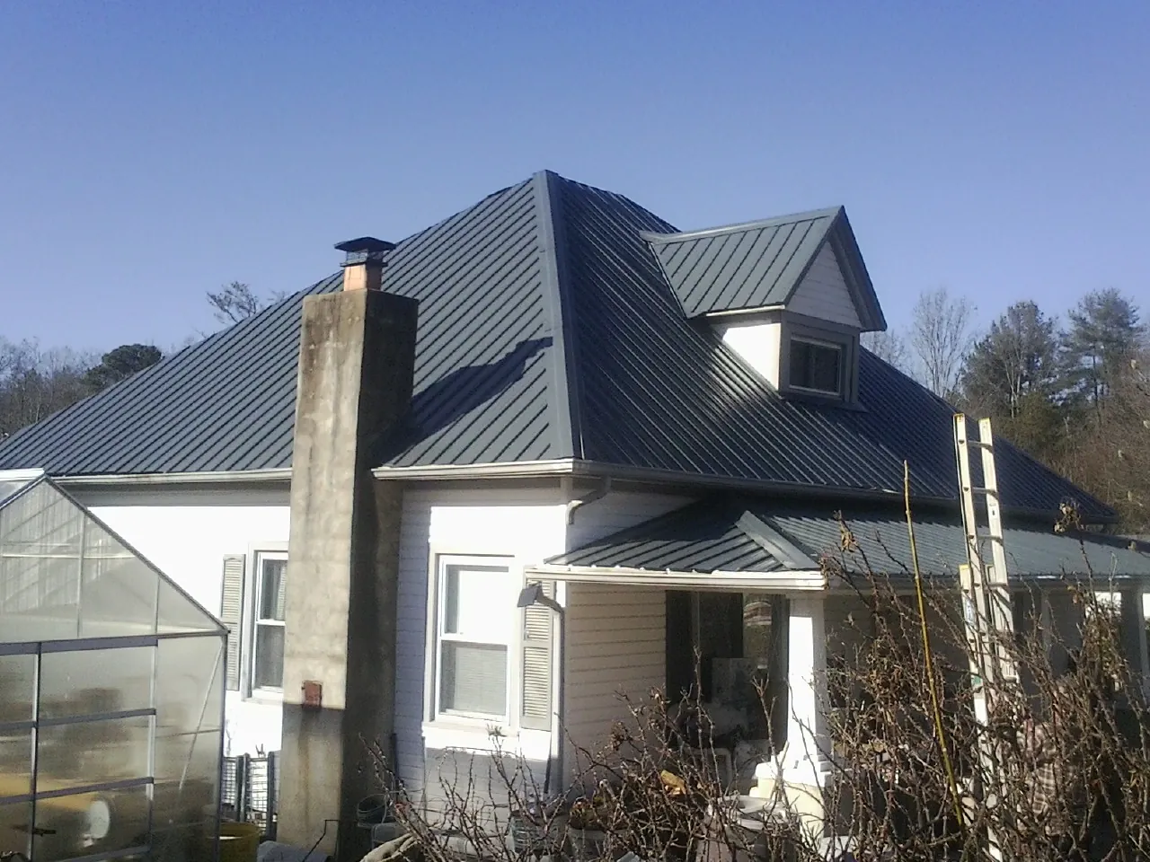 Dark blue standing seam metal roof on a white farmhouse with dormer — Slate & Tile Roof Repair by Roofing Brothers in Coram