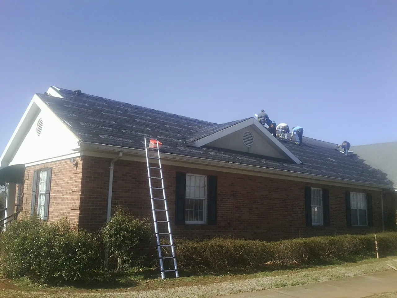 Crew tearing shingles off a brick ranch roof with a ladder set — Metal Roof Repair work by our crew in Coram