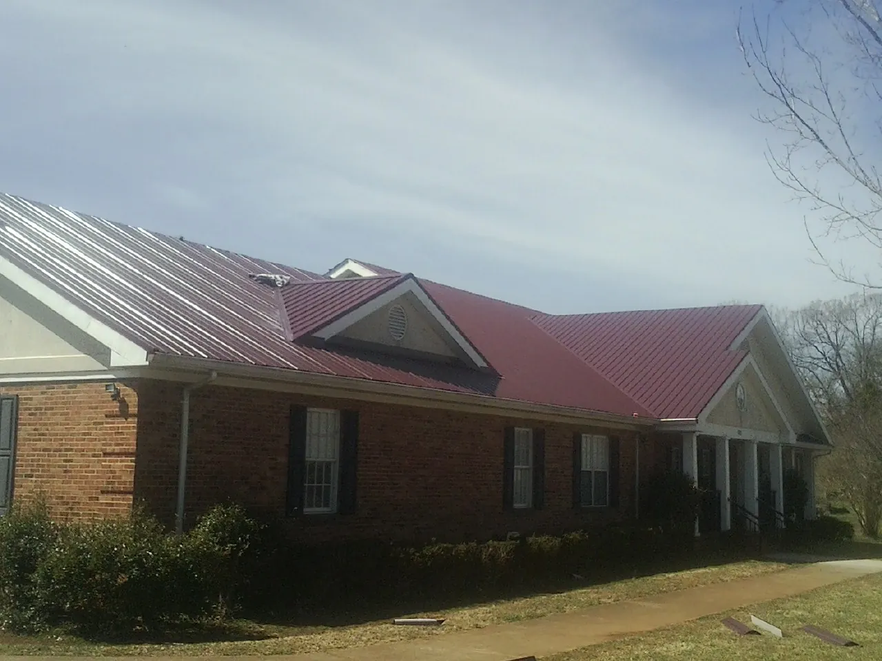 Red metal roof with gabled entries on a long brick building, from a Hail Damage Roof Repair job in Coram