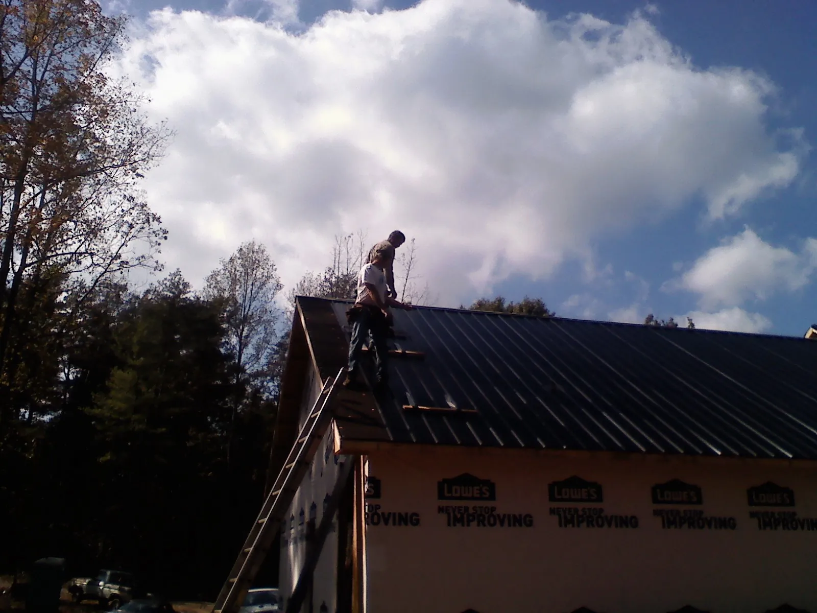 Roofer fastening dark metal panels high against a cloudy sky, from a Roof Inspection job in Coram