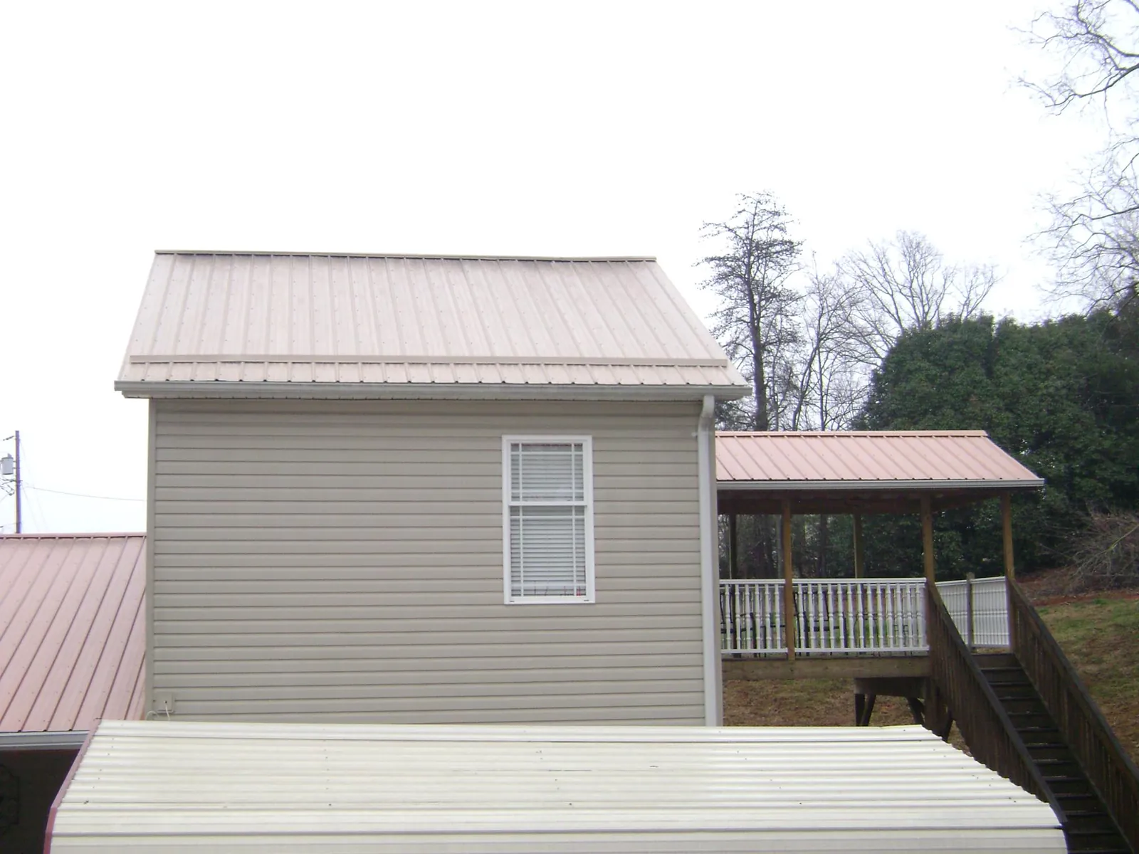 Tan metal roofs on a two story addition and attached porch, from a Roof Replacement job in Coram